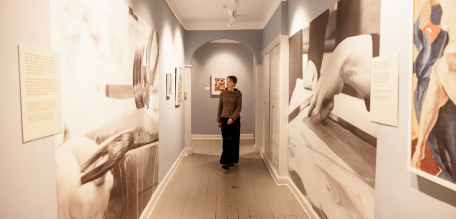 Eine Frau geht durch die Ausstellung Eine Collage – Franciska Clausen 125 Jahre im Schloss Brundlund