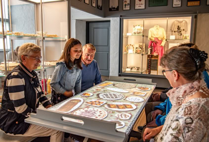 A few people are seated around a table, observing a digital installation that displays cakes
