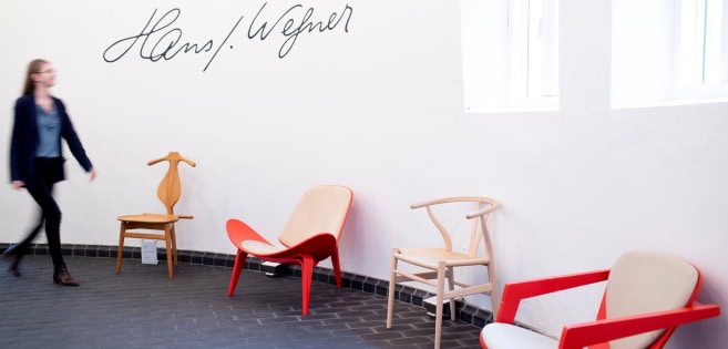 Eine junge Frau geht an die vielen Stühle von Hans J. Wegner vorbei