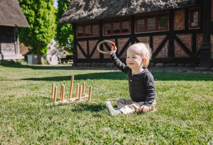 Ein kleiner Junge sitzt mit einem Spielzeug auf dem Gras im Freilichtmuseum Haderslev
